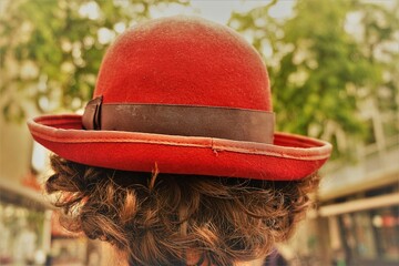 Hinterkopf von jungem Mann mit braunen Locken und rotem Filzhut auf Straße vor Häuserreihen,...