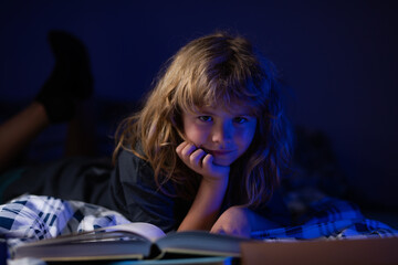 A little cute boy reading a book lying on the bed. Imagination or learning concept.