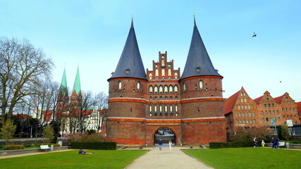 Lübeck Holstentor mit zwei Spitztürmen neben Salzspeichern und Grünanlage unter blauem Himmel