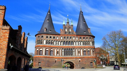 Obraz premium altes Lübecker Holstentor aus Backstein mit zwei Spitztürmen am Stadteingang unter blauem Himmel