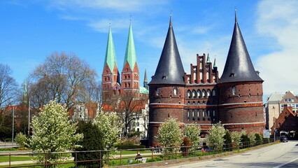 Obraz premium Lübeck Holstentor mit Spitztürmen und Kirchtürmen in Grünanlage unter blauem Himmel