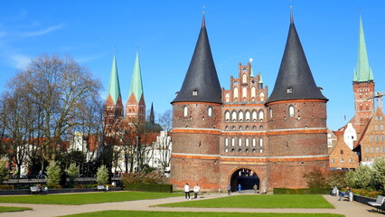 Fototapeta na wymiar Lübeck Holstentor mit Spitztürmen und Kirchtürmen in Grünanlage unter blauem Himmel