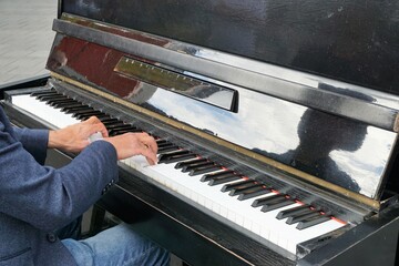 Spielende Hände auf Tastatur von Pianist an schwarzem Klavier mit Spiegelung auf Straße in Stadt...