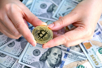 Bitcoin in female hands on US dollar banknotes background. Electronic decentralized money, exchange rate and growth of crypto currency