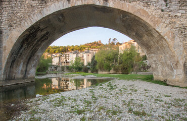 Fototapeta na wymiar Arche de pont au dessus de la Vidourle dans le Gard avec en arrière plan le village de Sauve dans le Gard