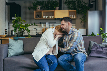 Pregnant woman at home sitting on sofa sad and crying, husband calms and supports, young married couple