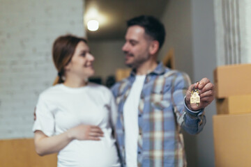 Close-up selective focus photo, man and pregnant woman together in new apartment smiling and happy holding house keys