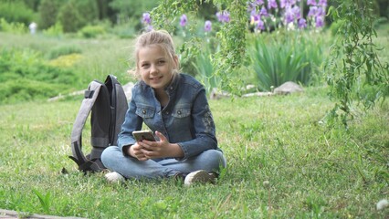 A pensive girl of nine years old, a schoolgirl, sits on the grass in the park.