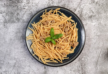 Mince meat pasta with basil leaves on a round plate on a dark gray background. Top view, flat lay