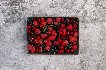 Ripe cherry, black currant, raspberry on a  rectangular   plate on a dark background. Top view, flat lay