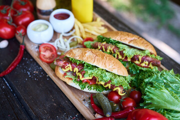 BBQ hot dog served with vegetables and French fries and sauces on wooden serving board