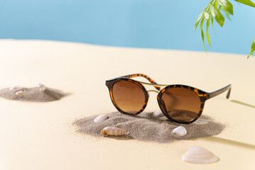 Womens Tortoiseshell frame sunglasses on a beach with palm leaf. Trendy sunglasses still life in...