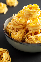 Homemade Organic Dry Tagliatelle Pasta in a Bowl on a black background, side view. Close-up.