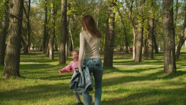 Little girl runs around happy mother joining hands in park