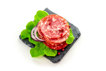 Salami sausage eats on a black slate plate with lettuce, spices . Isolated on a white background.