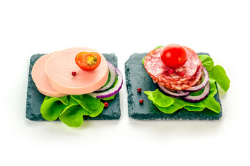 Boiled and salami sausage eats on a black slate plate with lettuce, spices and tomatoes. Isolated on a white background