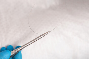 A podologist in blue gloves holds a titanium thread with tweezers. Close up. White background. The concept of podology and chiropody - obrazy, fototapety, plakaty