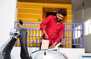 Young man talking out electric scooter battery from bike dicky for recharging near home - concept...