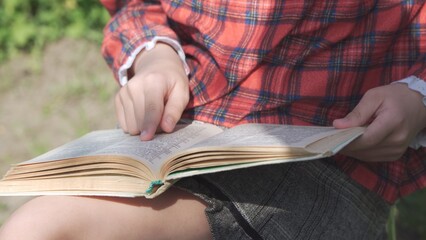 The book is in the hands of a girl who follows her finger over the text she is reading.