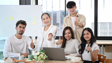 Successful business team showing thumbs up and looking at camera, support and team spirit together, celebrating corporate achievement