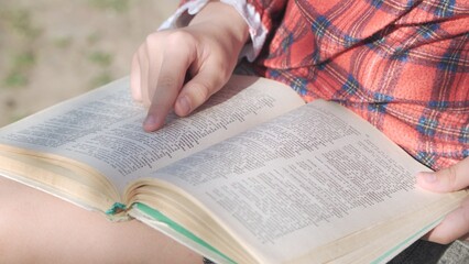 The book is in the hands of a girl who follows her finger over the text she is reading.