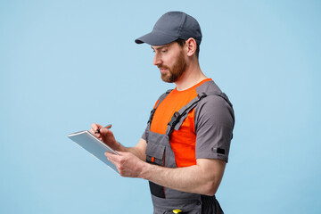 Focused Delivery man in uniform holding tablet and taking work notes