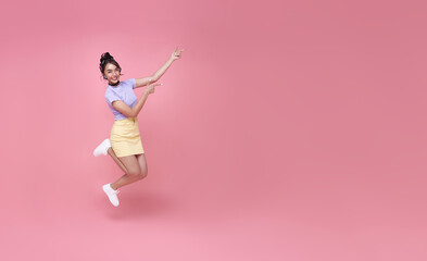 Fototapeta na wymiar Happy Asian woman smiling and jumping while hands pointing isolated over pink background. copy space
