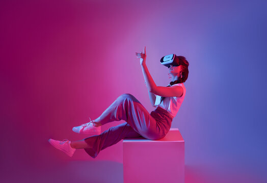 Amazed young woman using a virtual reality headset playing video games trying to touch something with hand floating in mid-air.