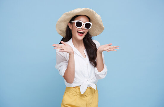 Happy beautiful Asian woman dressed in summer clothes smiling with open hand gesture of welcome isolated on blue background..