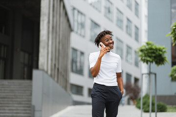 Side view portrait of smiling young african american woman walking and talking with mobile phone outside. Close up portrait of attractive young woman smiling and talking on smartphone.