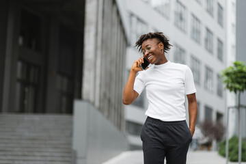 Side view portrait of smiling young african american woman walking and talking with mobile phone outside. Close up portrait of attractive young woman smiling and talking on smartphone.