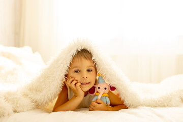 Obraz premium Little toddler child, cute kid with knitted small cute animal toy, lying in bed