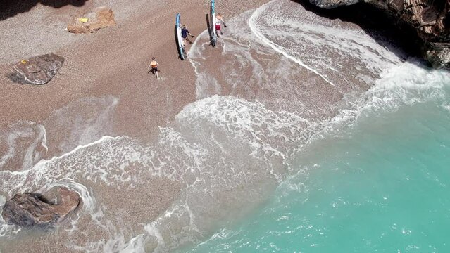 Aerial view of young adult man and woman go out of sea carrying paddle boards. Family aquatic activities