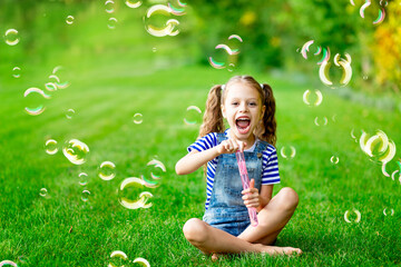 funny baby girl in the summer on the lawn with soap bubbles on the green grass, having fun and rejoicing, space for text