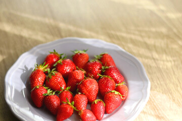 Lilac plate full of fresh strawberries on wooden table. Selective focus.