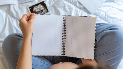 Baby list pregnant woman. Young pregnancy mother holding notepad. Pregnant lady writing check list...
