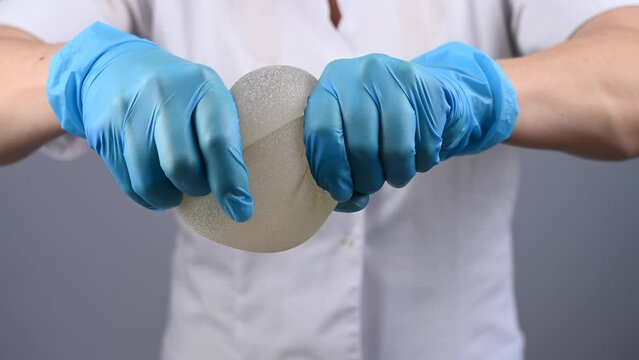 A plastic surgeon demonstrates the strength of silicone breast implants by squeezing them.