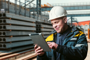 civil engineer with a tablet in his hands stands in the warehouse of finished products of a factory for the production of reinforced concrete products