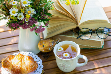 Bouquet of meadow flowers, croissant, cup of tea or coffee, books on table in summer garden. Rest in garden, reading books, breakfast, vacations in nature concept. Summertime in garden on backyard