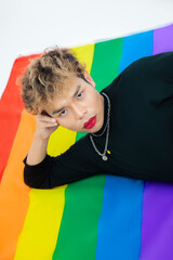 asian gay lay down on pride flag rainbow color background and looking at camera. lgbtq and lgbtq+ concept