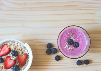 flat lay of  breakfast with a  glass of blueberry smoothie and oat or granola in white bowl, fresh blueberries, strawberries on wooden table. Healthy breakfast concept.