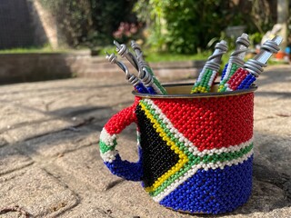 A close up view of a tin cup with south african beads wrapped around it with the south african...