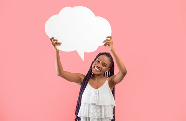 Cheery young African American woman holding empty speech bubble with mockup on pink studio background