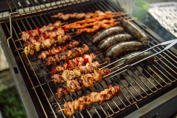 Closeup view of a hot food vendor cooking pork sausages and chops over a hot grill with rising steam, chef uses tongs to flip meat at local agricultural fair