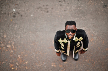 Mega stylish african man in traditional jacket pose. Fashionable black guy in sunglasses with cigar.