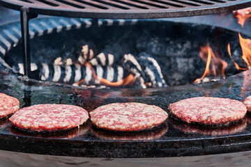 Raw burger patties are grilled on barbecue on open fire at in park.
