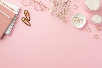 Fototapeta na wymiar Business concept. Top view photo of workplace candles diaries pencils stylish glasses gold rings barrettes and white gypsophila flowers on isolated pastel pink background with empty space