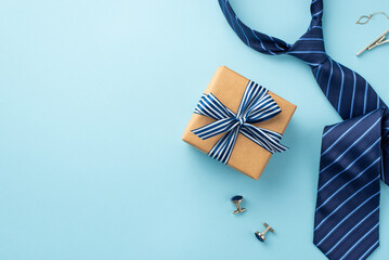 Father's Day concept. Top view photo of craft paper giftbox with ribbon bow tie clip cufflinks and blue necktie on isolated pastel blue background with copyspace