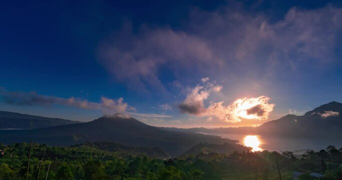 Timelapse of sunrise with view on volcanoes and lake on Bali. Clouds are moving fast in blue sky, the sun is rising
