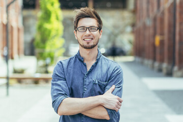 Portrait of a young teacher on campus, man with arms crossed smiling and looking at camera with beard and glasses